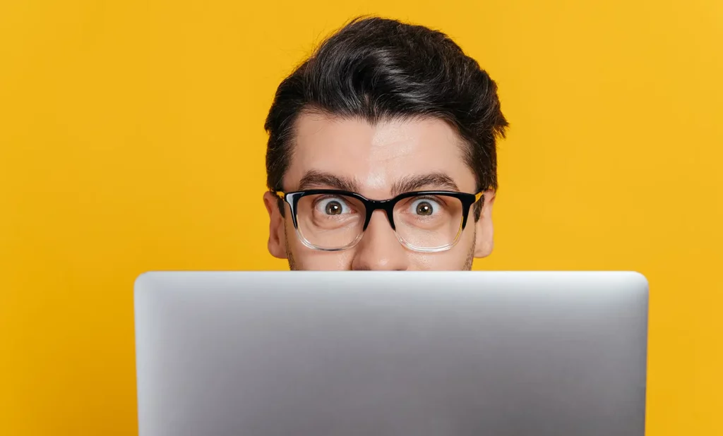 Surprised man peering over the top of his laptop screen